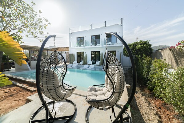 A modern house with a pool, two hanging chairs, and a garden.