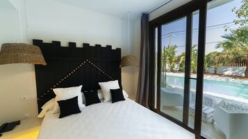 Habitación de hotel con una cama, cabecera negra, dos lámparas y vista a una piscina a través de ventanas amplias.