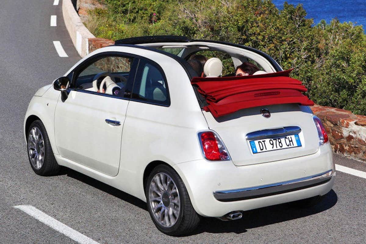 Un coche blanco con portaequipajes rojo aparcado en una carretera.