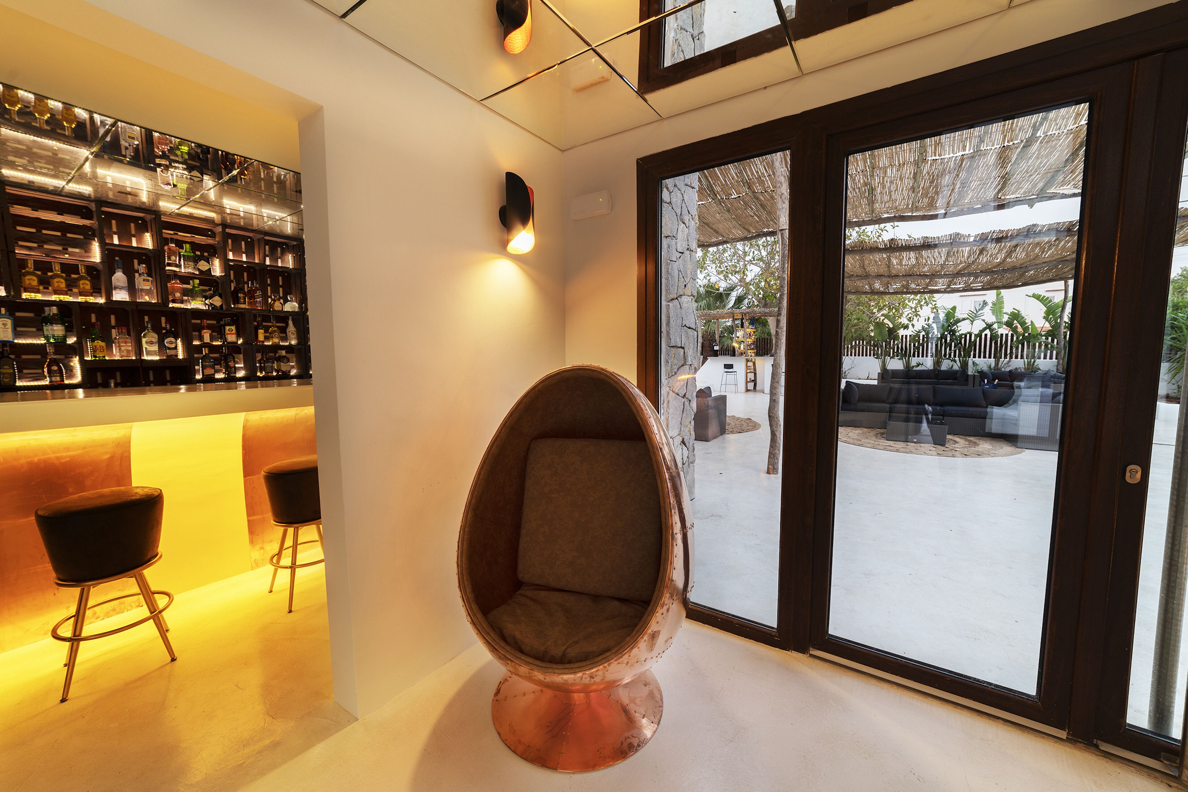 Un interior moderno con una zona de bar, una silla de cobre original y vistas del patio exterior.