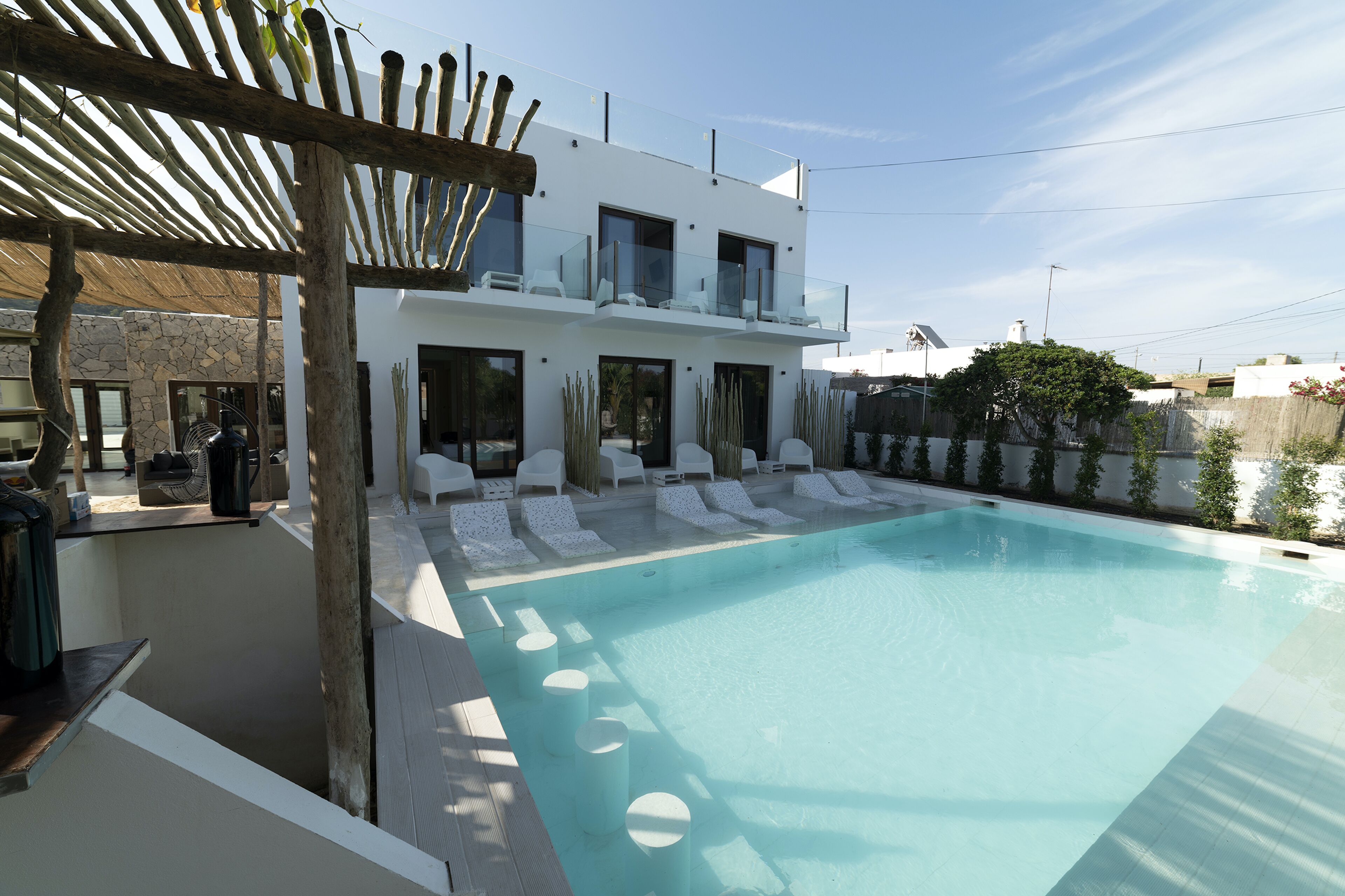 A modern two-story house with a swimming pool, white lounge chairs, and a pergola.