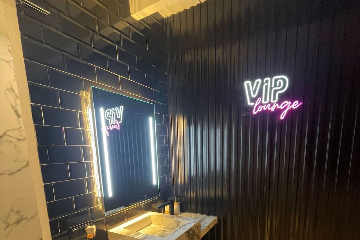 Un baño moderno con dos lavabos, encimeras de mármol y un letrero de neón que dice 