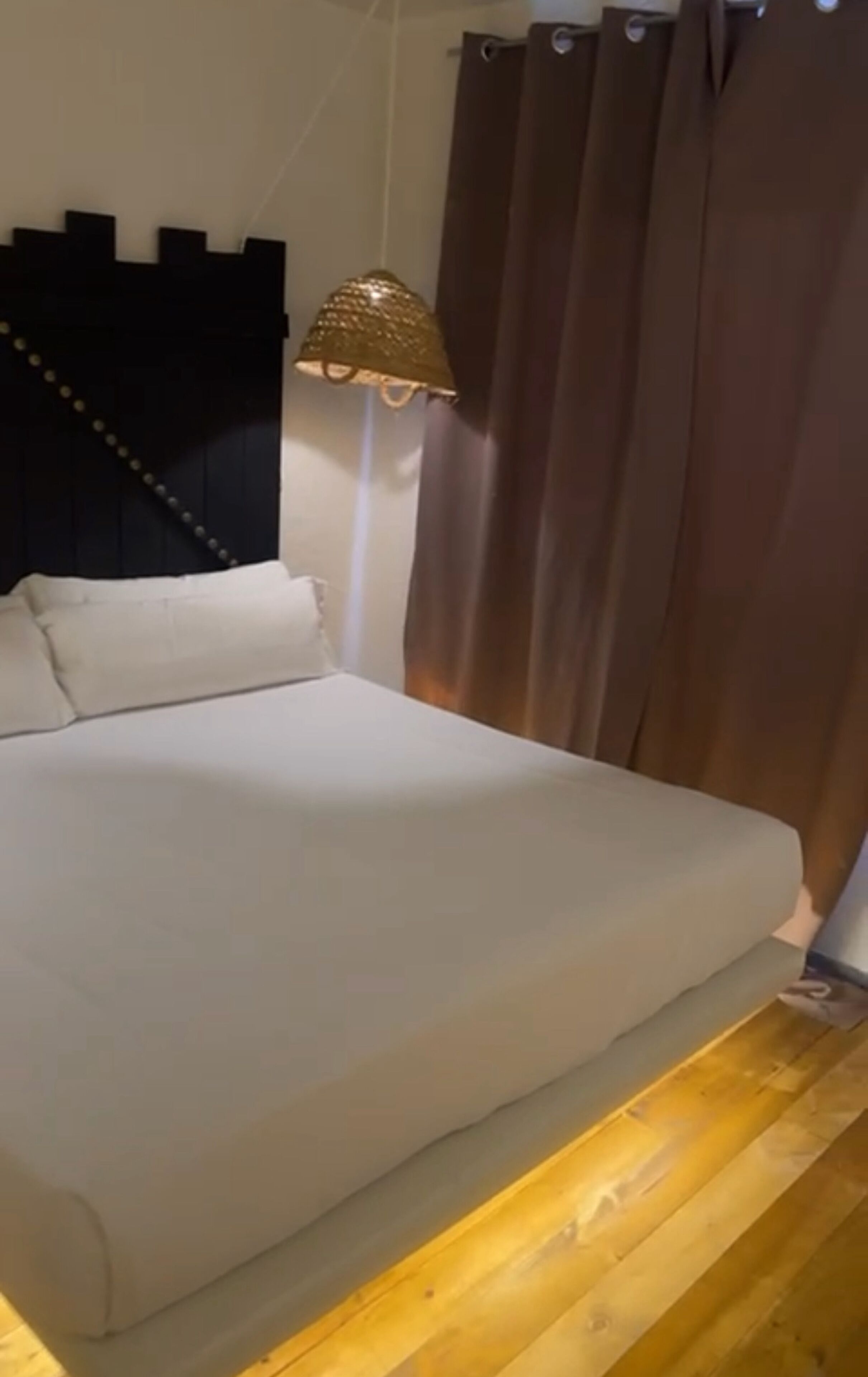 Una cama con cabecera, lámpara y cortinas.