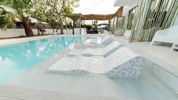 Una piscina con solárium de baldosas y zona de estar cubierta.