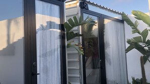 Un edificio moderno con grandes puertas de vidrio, una escalera visible y un balcón con plantas.