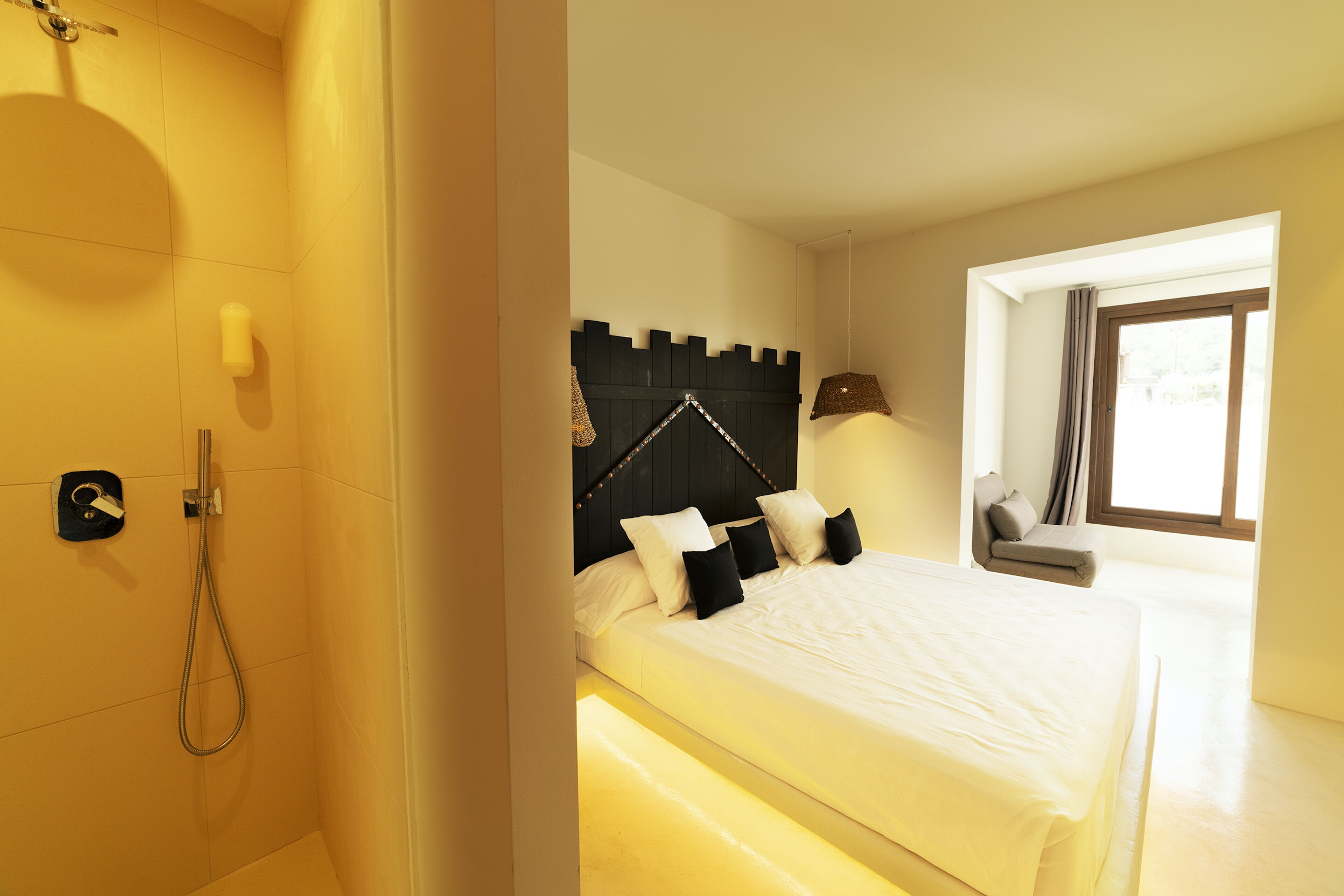 Een slaapkamer met een bed, nachtkastje, lamp, raam en douchegedeelte.