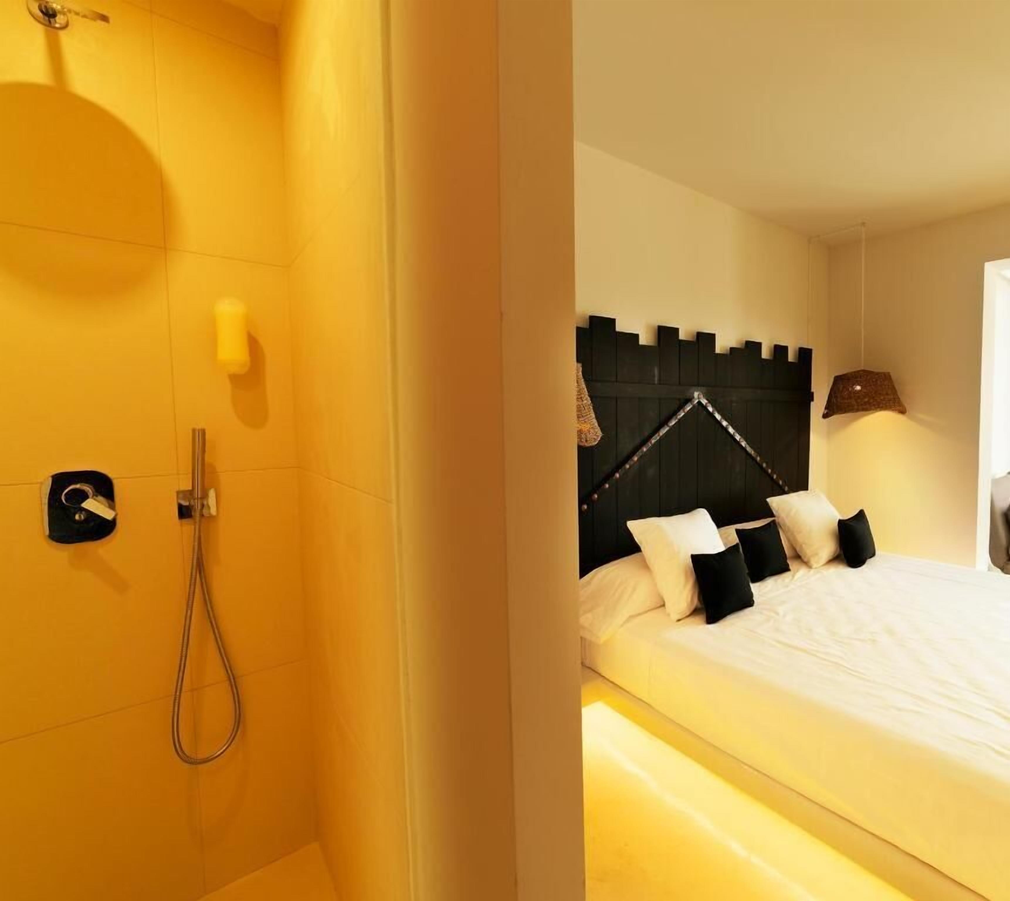 A hotel room with a shower, a bed with white bedding and black pillows, and a headboard with a unique design.