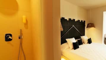 A hotel room with a shower, a bed with white bedding and black pillows, and a headboard with a unique design.