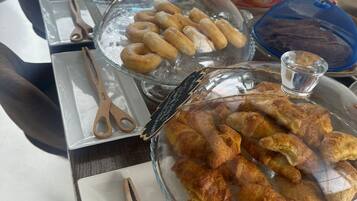 Une table de buffet proposant une variété de plats, notamment des pâtisseries et du pain, présentés sous des cloches en verre et accompagnés d’ustensiles de service.
