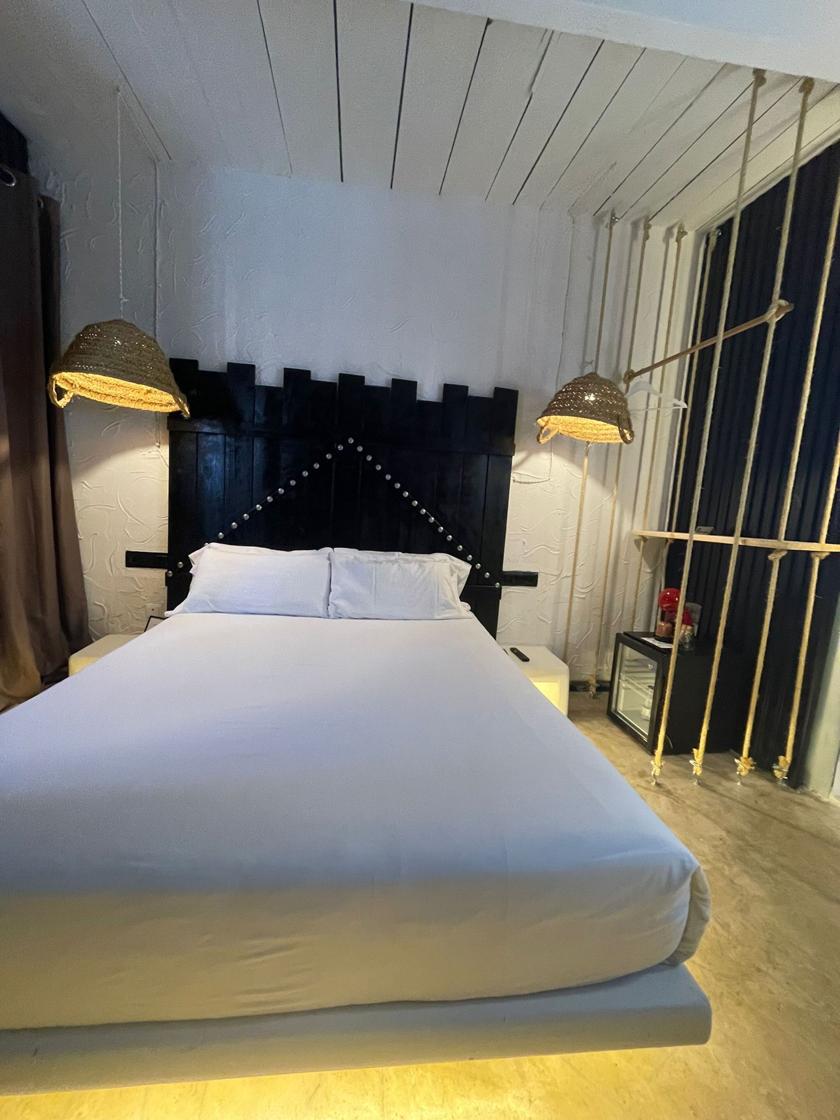 Una cama bien hecha con un cabecero negro y dos lámparas a cada lado.