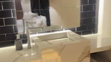 Un baño con lavamanos de mármol, un espejo y pared revestida de baldosas negras.