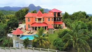 A large, multi-story building with a red roof, surrounded by lush greenery and a pool. - Captivating Mountain Views, Ocean Views,  Romantic getaway (Anse La Raye)