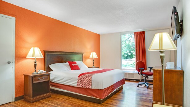 A hotel room with a large bed, two bedside tables with lamps, a desk with a chair, and a window with curtains.
