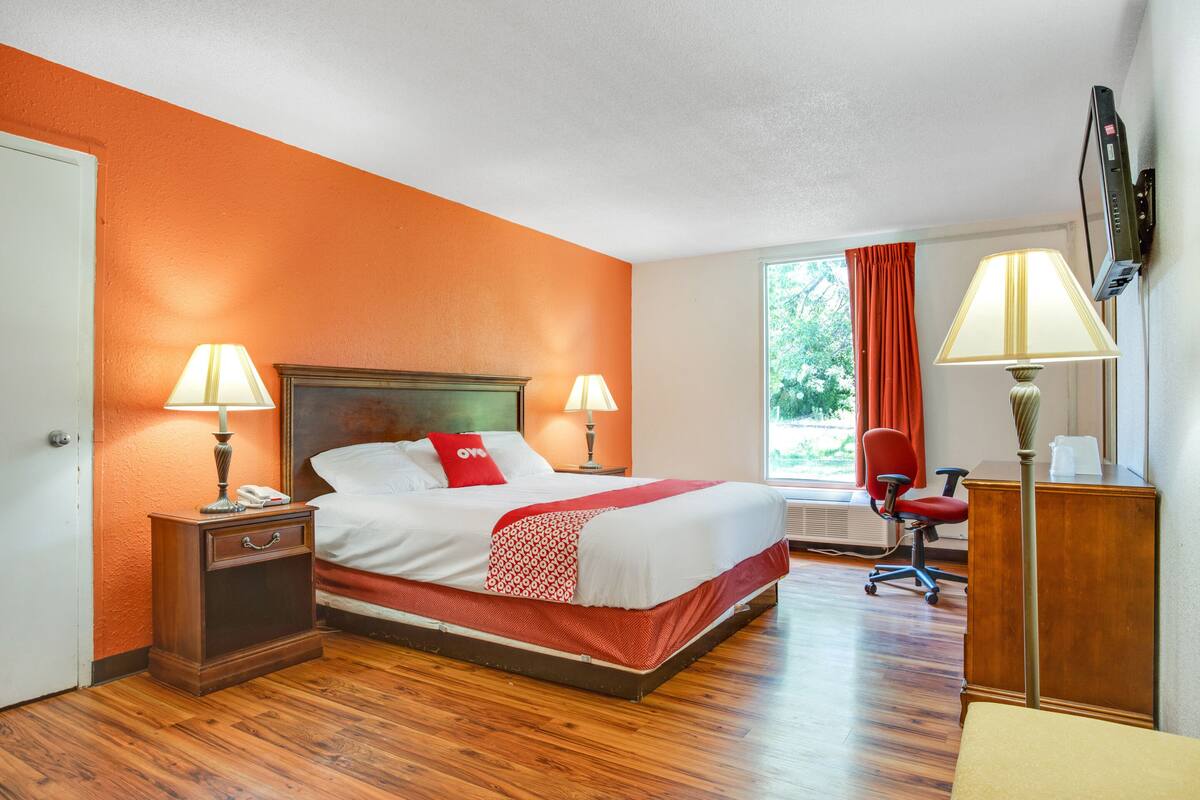 A hotel room with a large bed, two bedside tables with lamps, a desk with a chair, and a window with curtains.