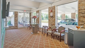 A reception area with a patterned carpet, a glass table with chairs, a brick wall, and a car parked outside.