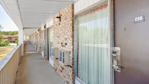A hotel corridor with a brick wall, a door with a number plate, and air conditioning units.