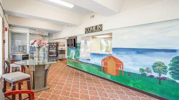 Un espace d'accueil avec une table en verre, des chaises, un vase de fleurs, une fresque représentant un paysage et une pancarte indiquant « ENTREZ ».