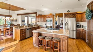 A spacious kitchen with wooden cabinets, a large island with stools, stainless steel appliances, and a wooden ceiling. - 10-Acre Mid-Valley Retreat with Hot Tub, Game Room & Sopris Views (Carbondale)
