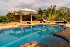 A swimming pool with lounge chairs and a covered seating area.