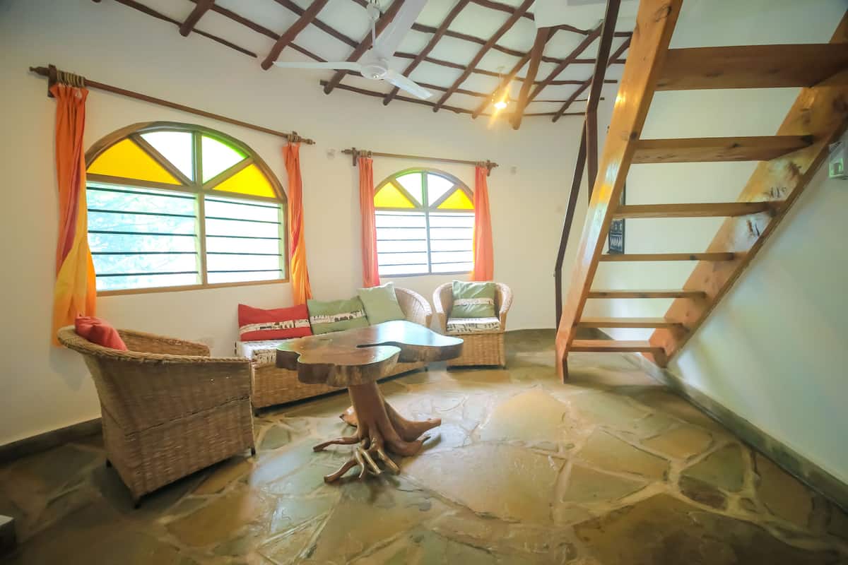 Una habitación acogedora con suelo de piedra, muebles de mimbre y una escalera de madera.