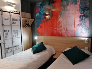 Habitación de hotel con dos camas, un cuadro abstracto de colores en la pared y un armario con etiquetas de capacidad de peso.