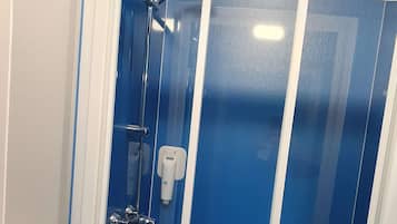 Une cabine de douche fermée par des parois en verre, dotée d’une porte blanche, d’un pommeau de douche à main et d’un distributeur de savon à main.