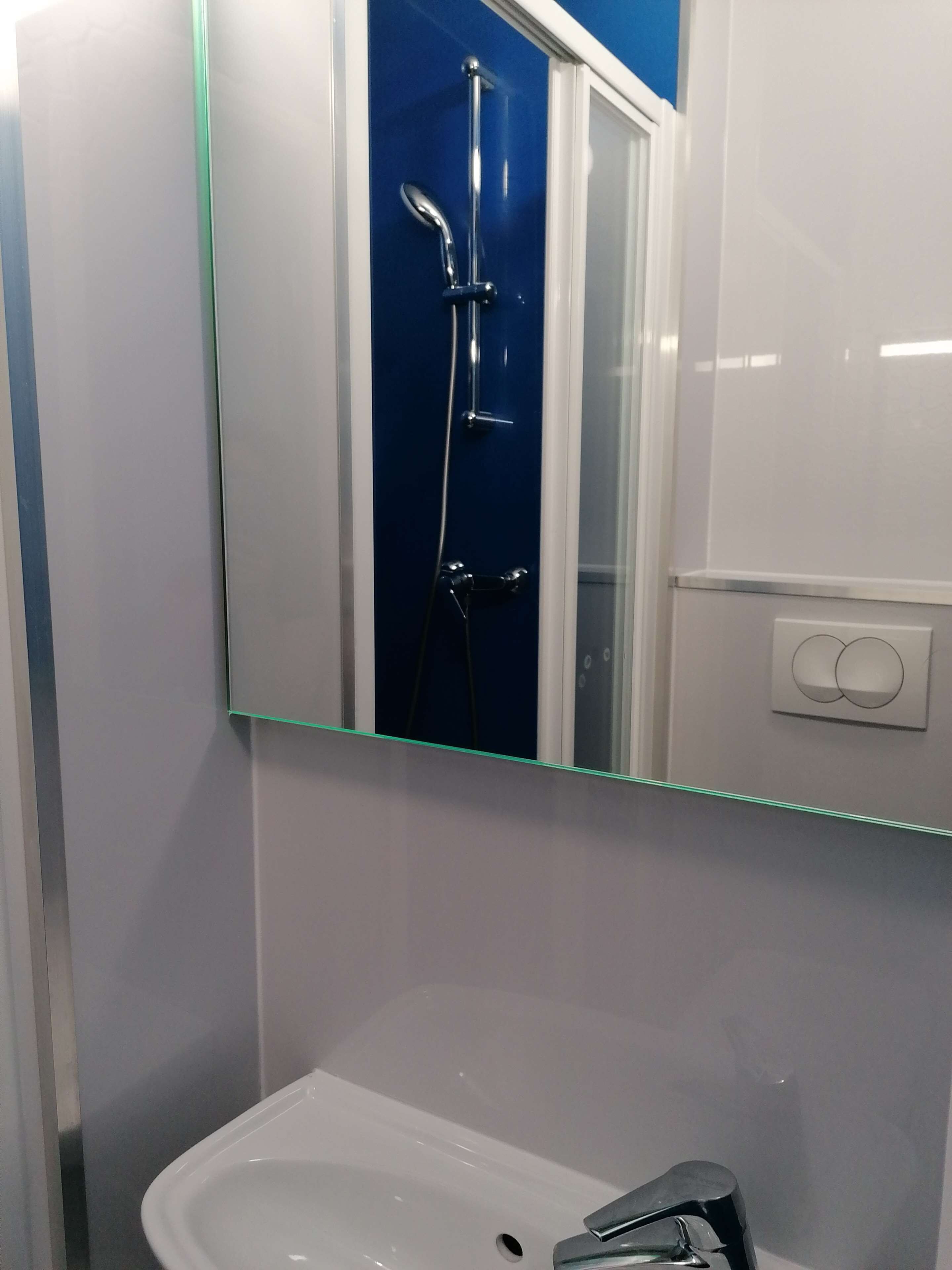 A bathroom with a white sink, a mirror, and a shower with a chrome fixture.