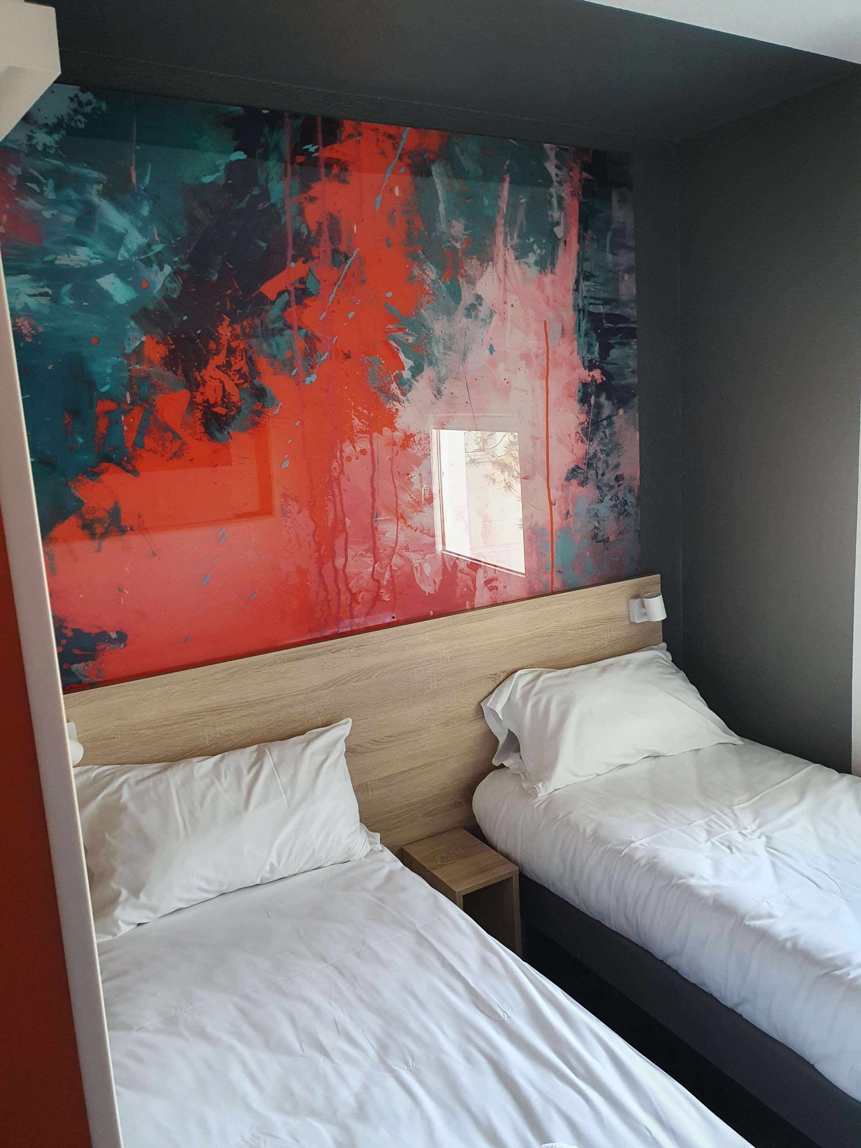A room with two beds, a wooden headboard, and a colorful abstract painting on the wall.