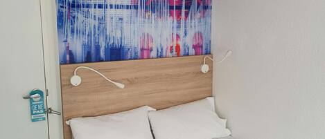 Une chambre d’hôtel avec un lit, du linge de lit blanc, une tête de lit en bois et un grand tableau abstrait accroché au mur.