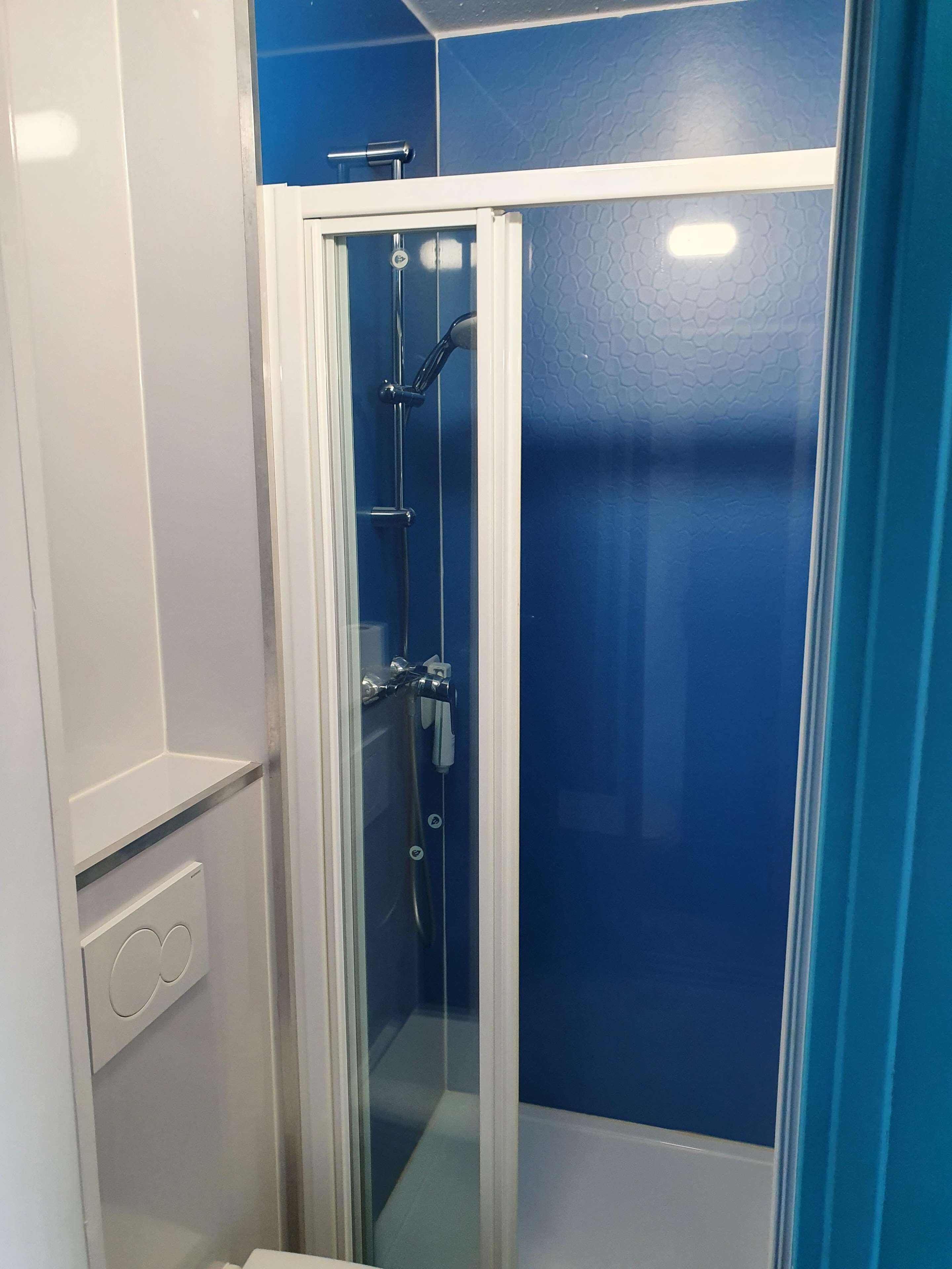 Een badkamer in hoekopstelling met een douchecabine van glas, witte wanden en een blauwe accentmuur.
