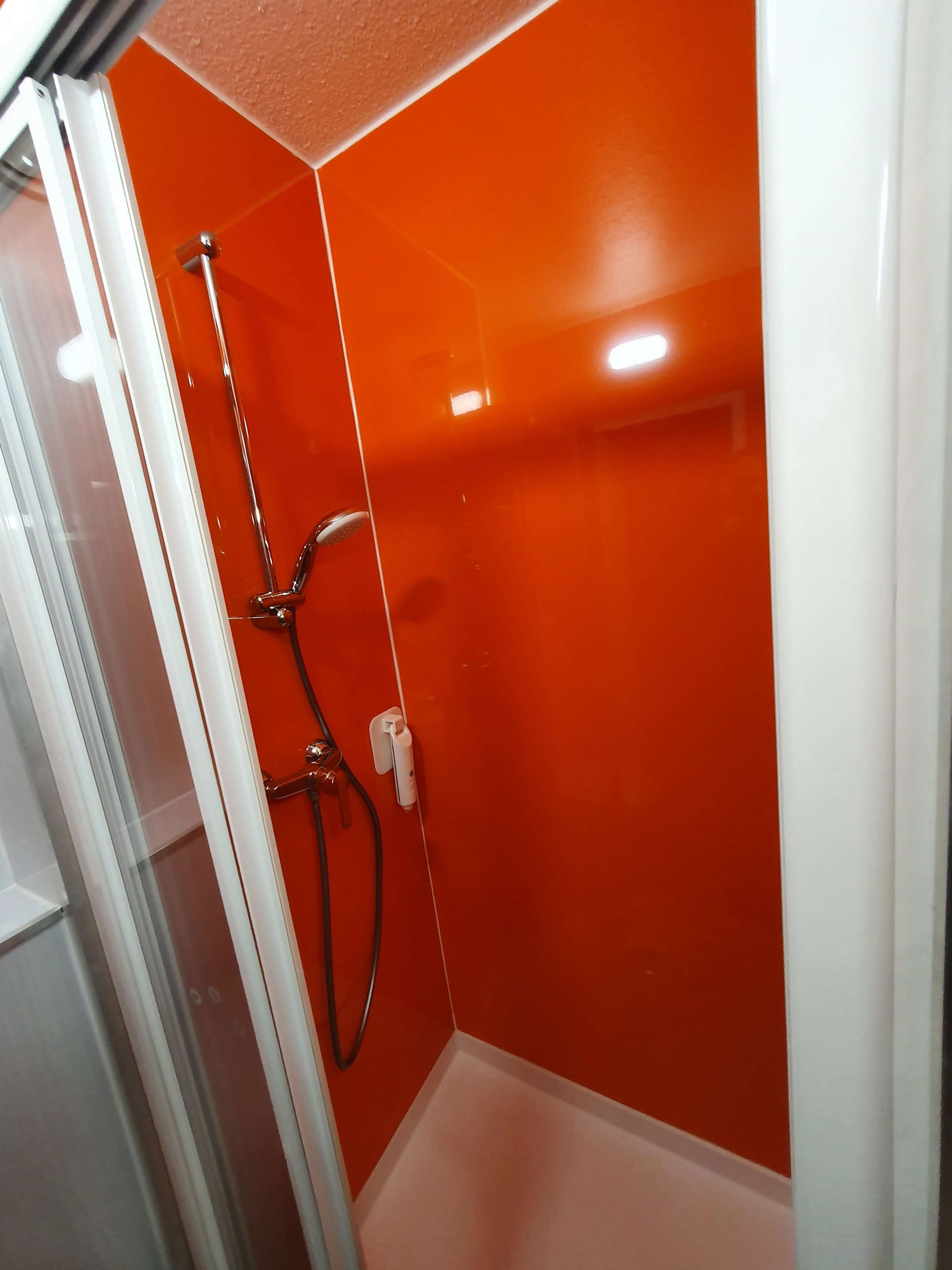 A bathroom with a glass door, a shower with a chrome handle, and a white bathtub.