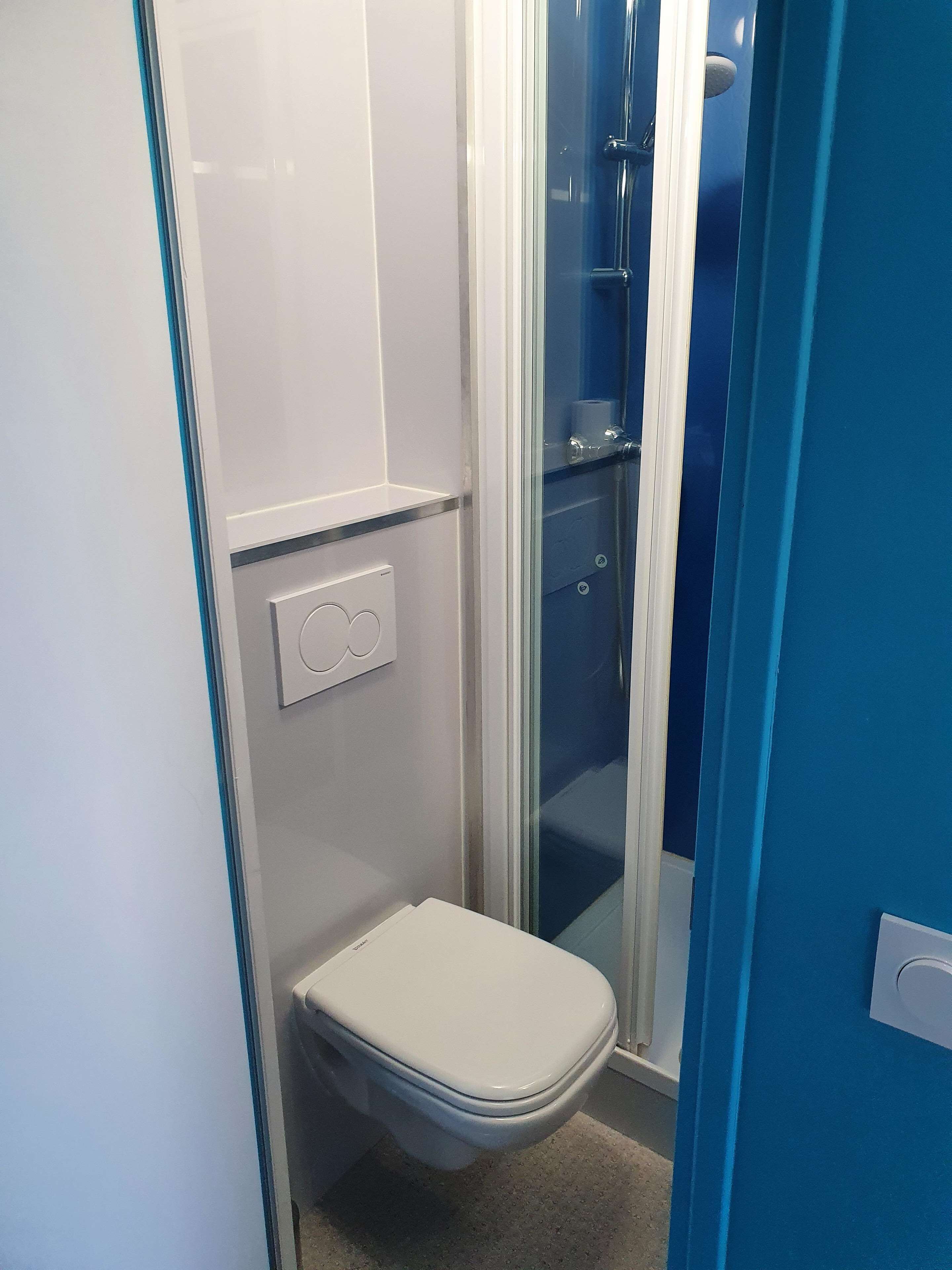 A compact bathroom with a toilet, a shower enclosure, and a wall-mounted flush handle.