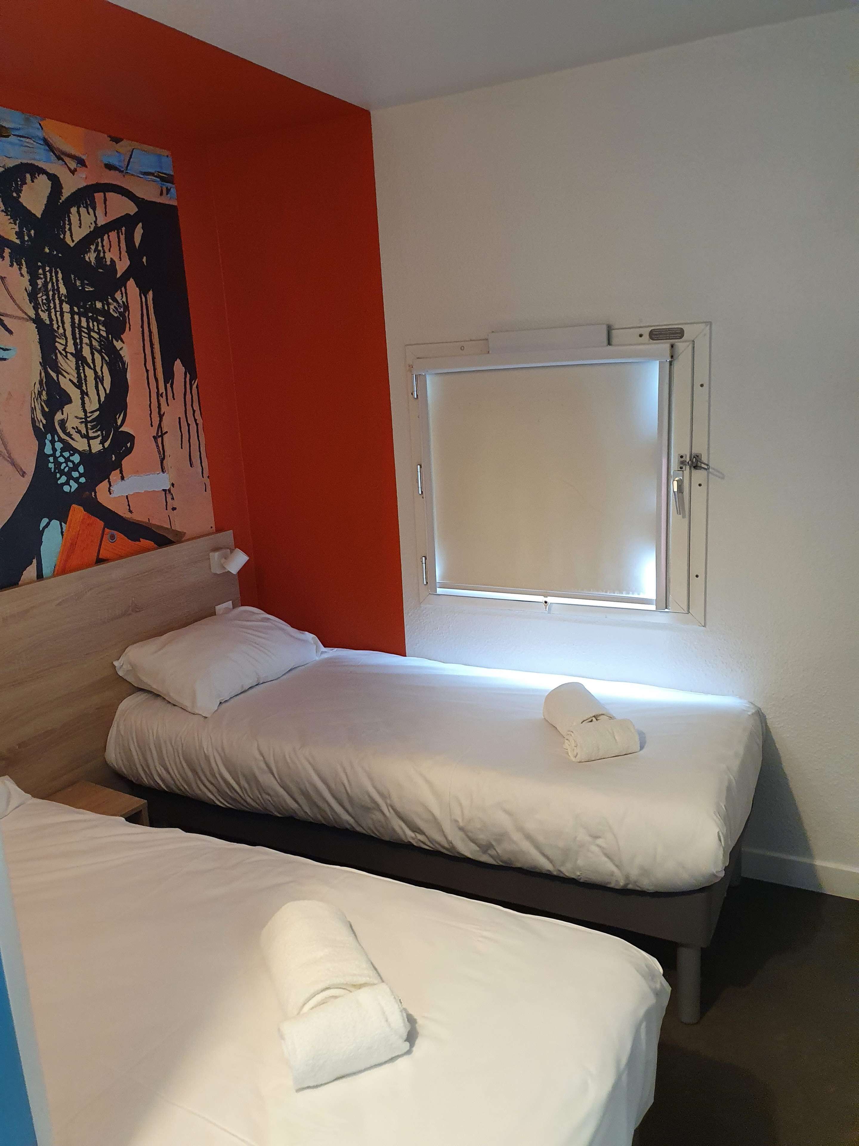A hotel room with two beds, a window, and a painting on the wall.