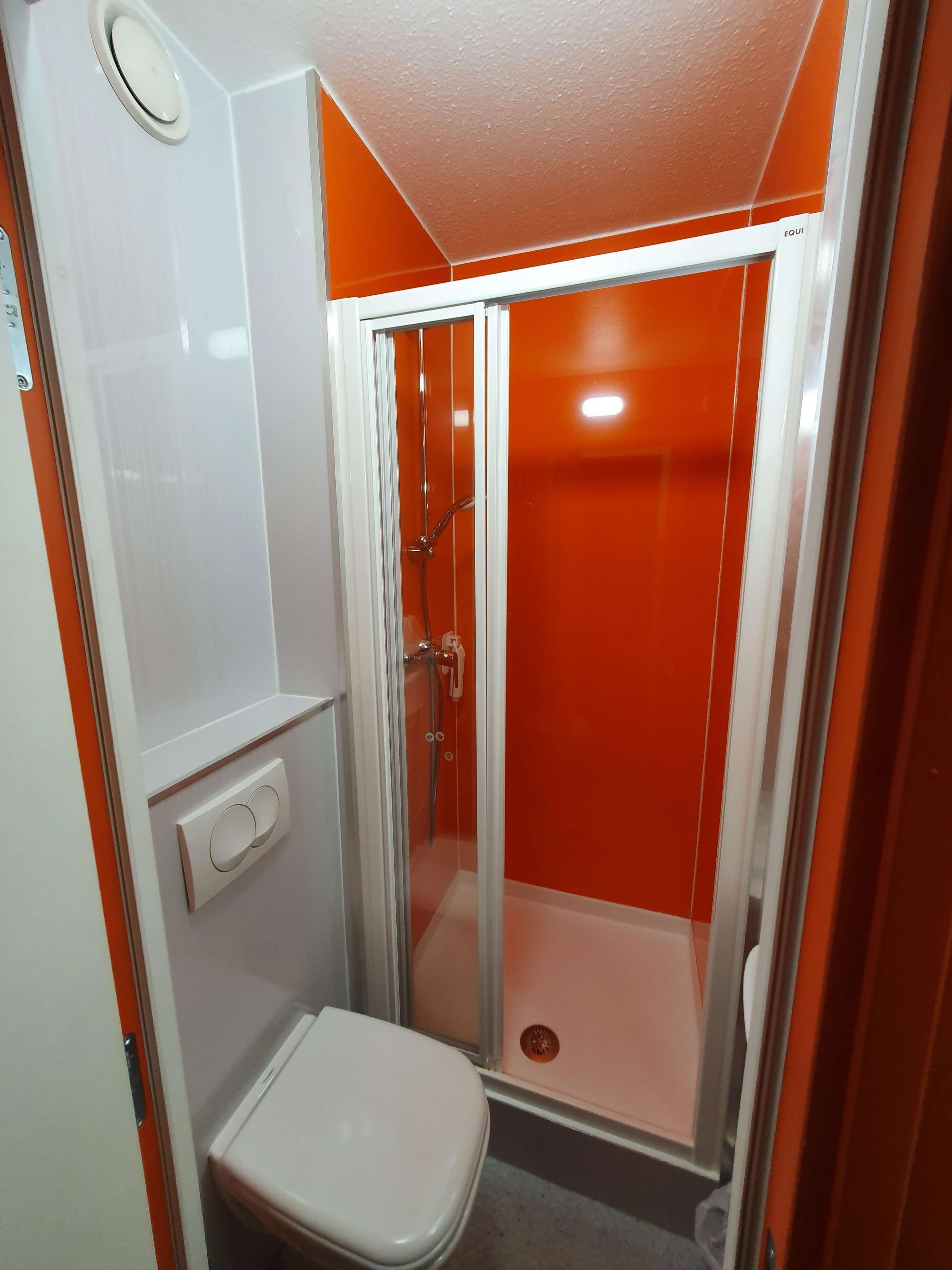 Une salle de bain compacte comprenant un espace douche, des toilettes et un panneau de commande fixé au mur.