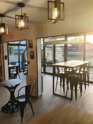 An indoor dining area with wooden tables and chairs, large windows, and hanging pendant lights. - KYRIAD DIRECT ORLEANS - Olivet - La Source (Olivet)