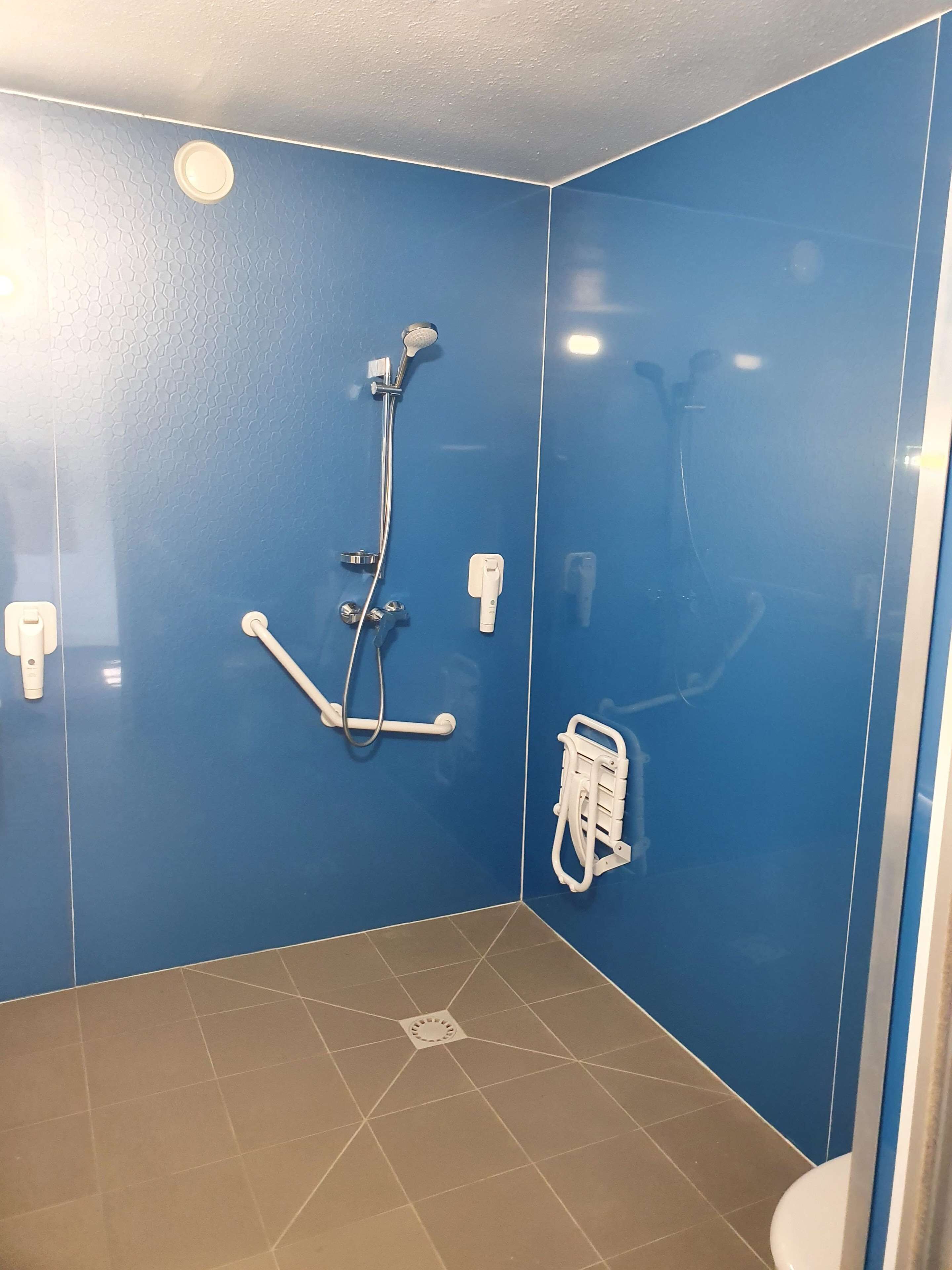 Une petite salle de bain aux murs bleus, équipée d’une douche, de toilettes et d’un sèche-mains.