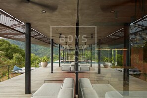 A modern outdoor lounge area with seating and potted plants, overlooking a lush landscape. - Atelier NEW design creation at Art Villas (Uvita)
