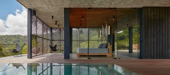 A modern outdoor lounge area with a pool, wooden deck, and a sofa with cushions. - Atelier NEW design creation at Art Villas (Uvita)