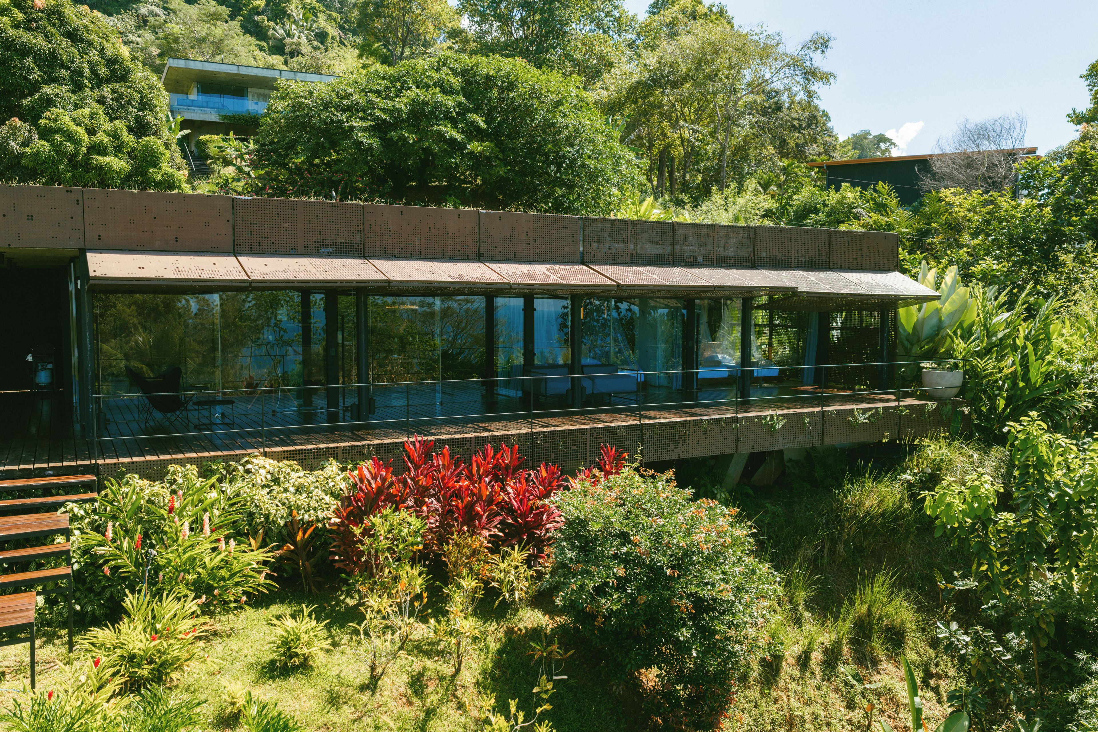 En moderne bygning med en glasfacade, et overdækket gangareal og frodig vegetation omkring.