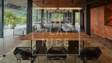 A modern dining area with a wooden table and black chairs, a large potted plant, and a view of lush greenery.