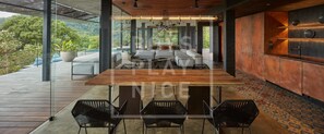 A modern dining area with a wooden table and black chairs, a large potted plant, and a view of lush greenery. - Atelier NEW design creation at Art Villas (Uvita)