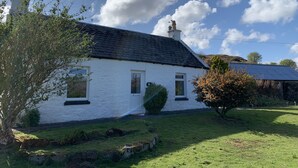 A white house with a black roof, surrounded by a grassy yard and a tree. - Heatherland Cottage (Skeabost)