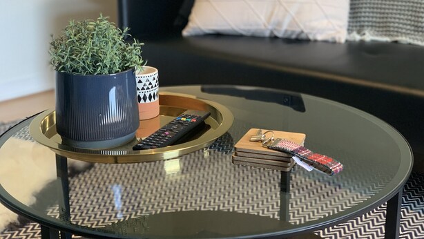 A modern living room with a glass coffee table, a potted plant, a remote control, and a decorative tray. - Heatherland Cottage (Skeabost)