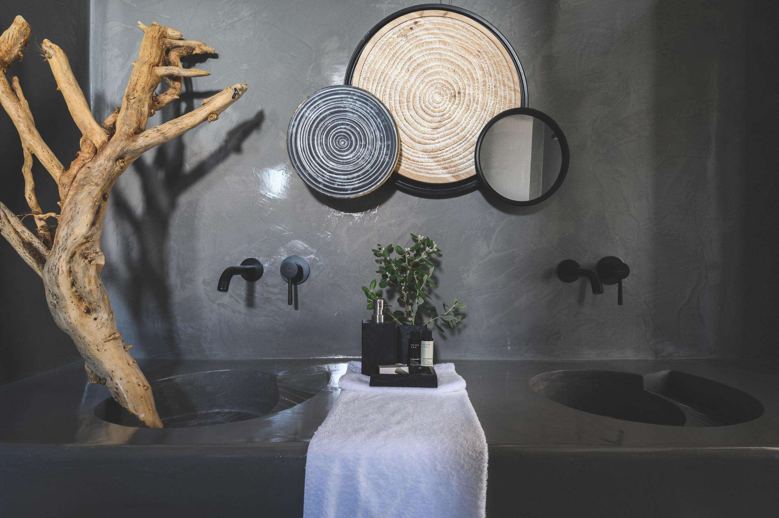 Un baño con un espejo grande, dos espejos más pequeños, una rama de madera, una toalla y una planta sobre una estantería.