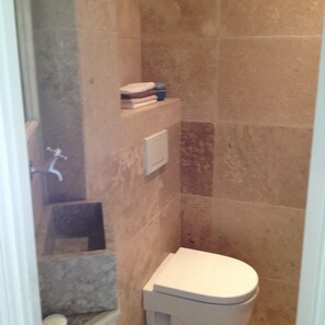 A small bathroom with a toilet, a shelf with toiletries, and a shower area.