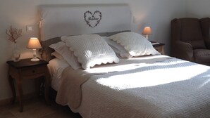 Un lit bien fait, agrémenté d’une décoration en forme de cœur sur la tête de lit, deux lampes de chevet et une chaise placée dans un coin.