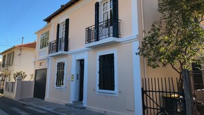 Un immeuble de deux étages avec une façade beige, des volets noirs et un balcon orné de rampes en métal ouvragé.