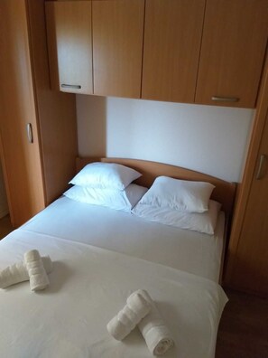 A neatly made bed with white linens and pillows, a wooden headboard, and two rolled towels on the bed.