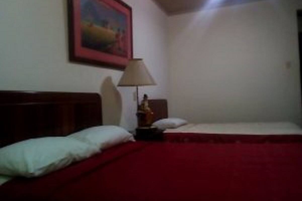 Una habitación con una cama individual, una mesita de noche con una lámpara y un cuadro en la pared.