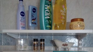 A bathroom shelf with various toiletries including a bottle of Nivea, a bottle of Vidal, a bottle of baby shampoo, and a jar of Botanique Therapy. - Palinas comfy home!! (Kalamata)